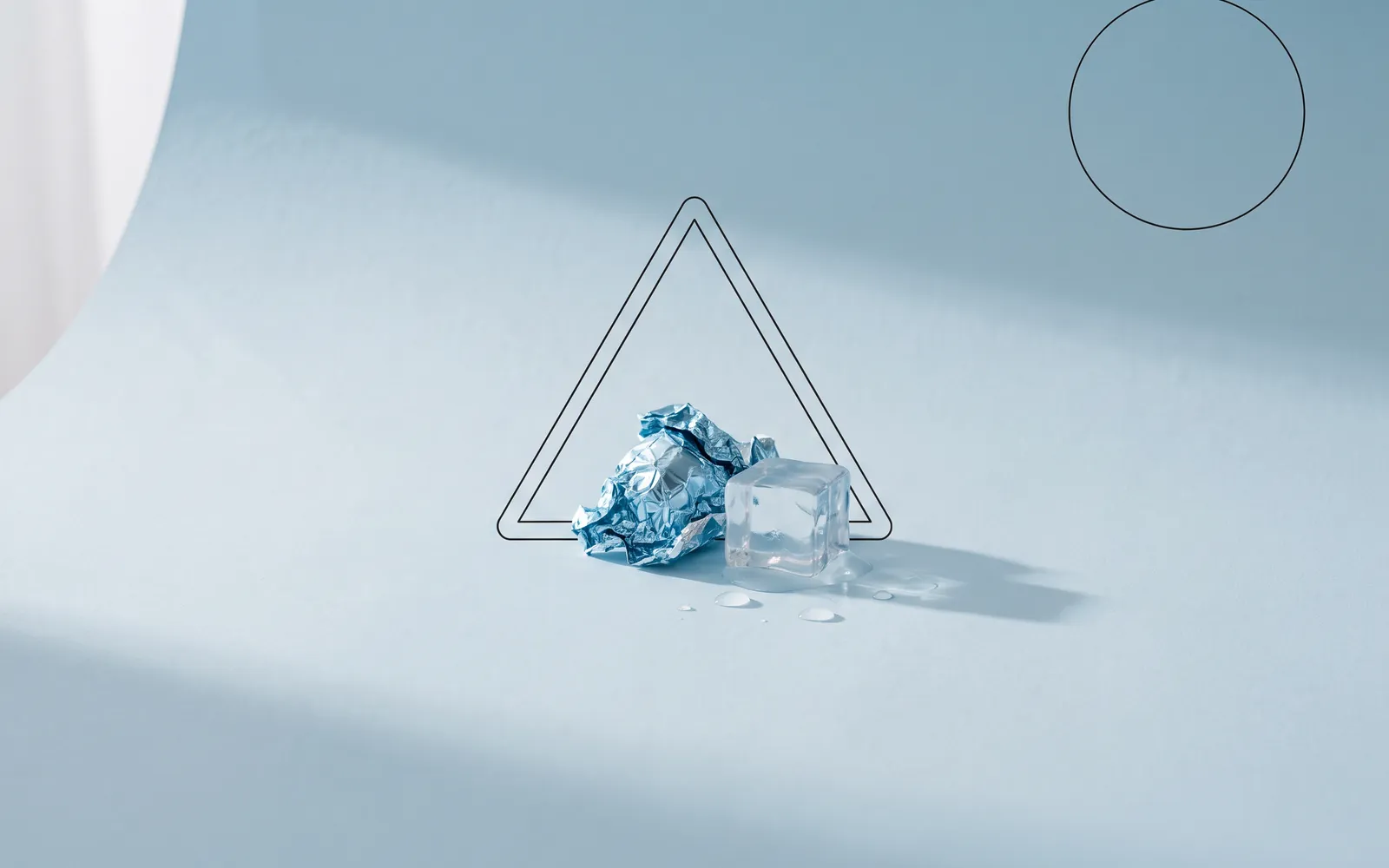 Stillleben: zerknitterte blaue Folie und schmelzender Eiswürfel, dahinter ein feines Warndreieck.