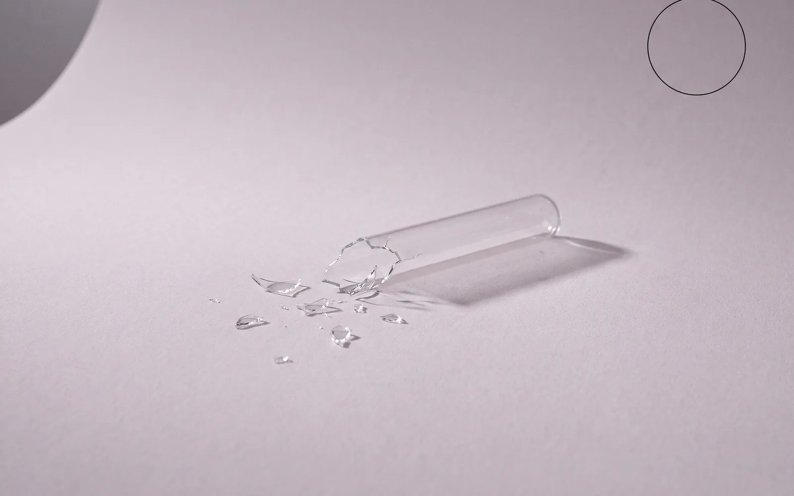 Stillleben: ein zersplittertes Glasröhrchen auf hellem Papier vor Mauve, darüber ein feiner Kreis.