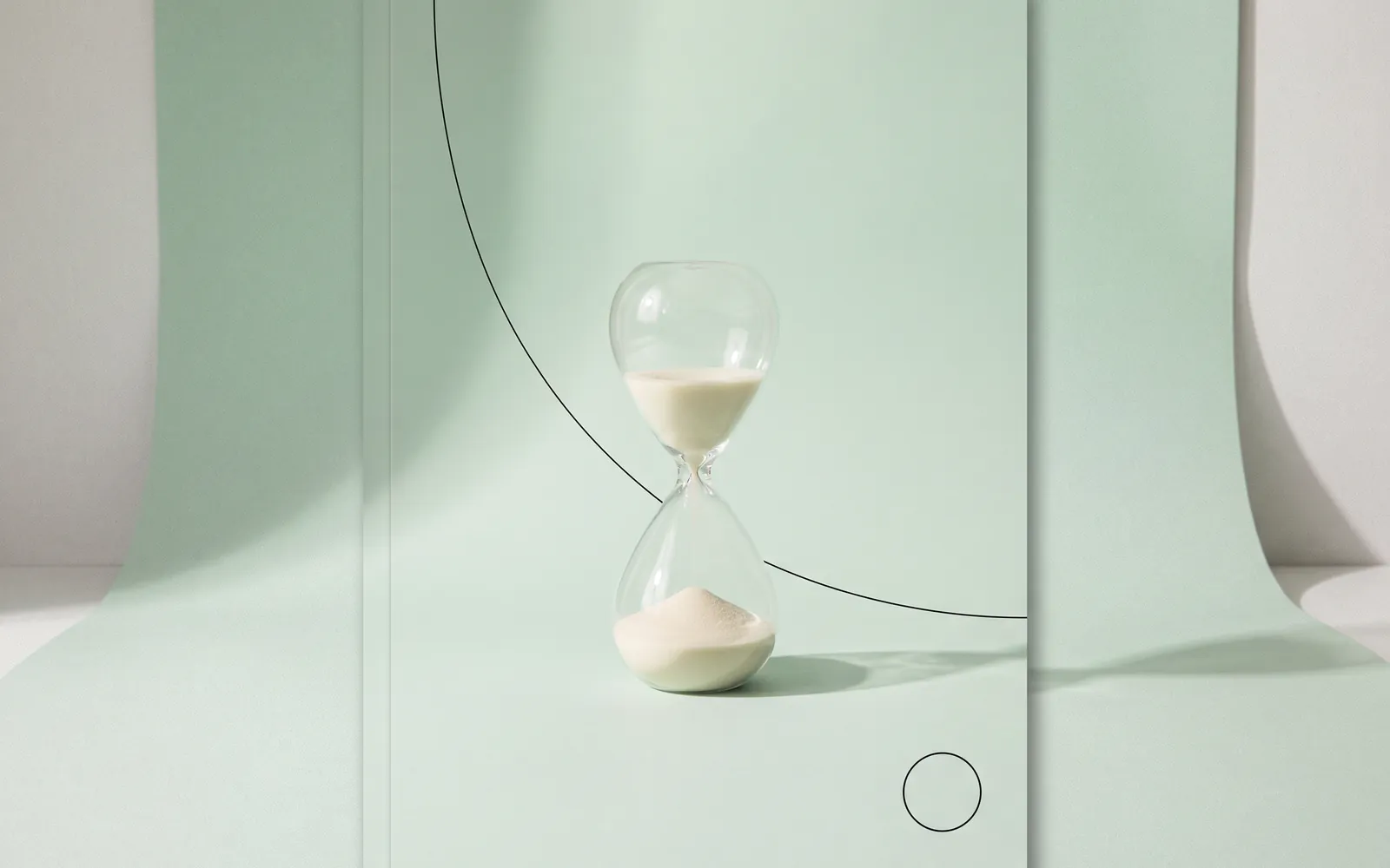 Stillleben: eine Sanduhr mit hellem Sand vor mintgrünem Papier, daneben ein feiner Bogen und ein kleiner Kreis.