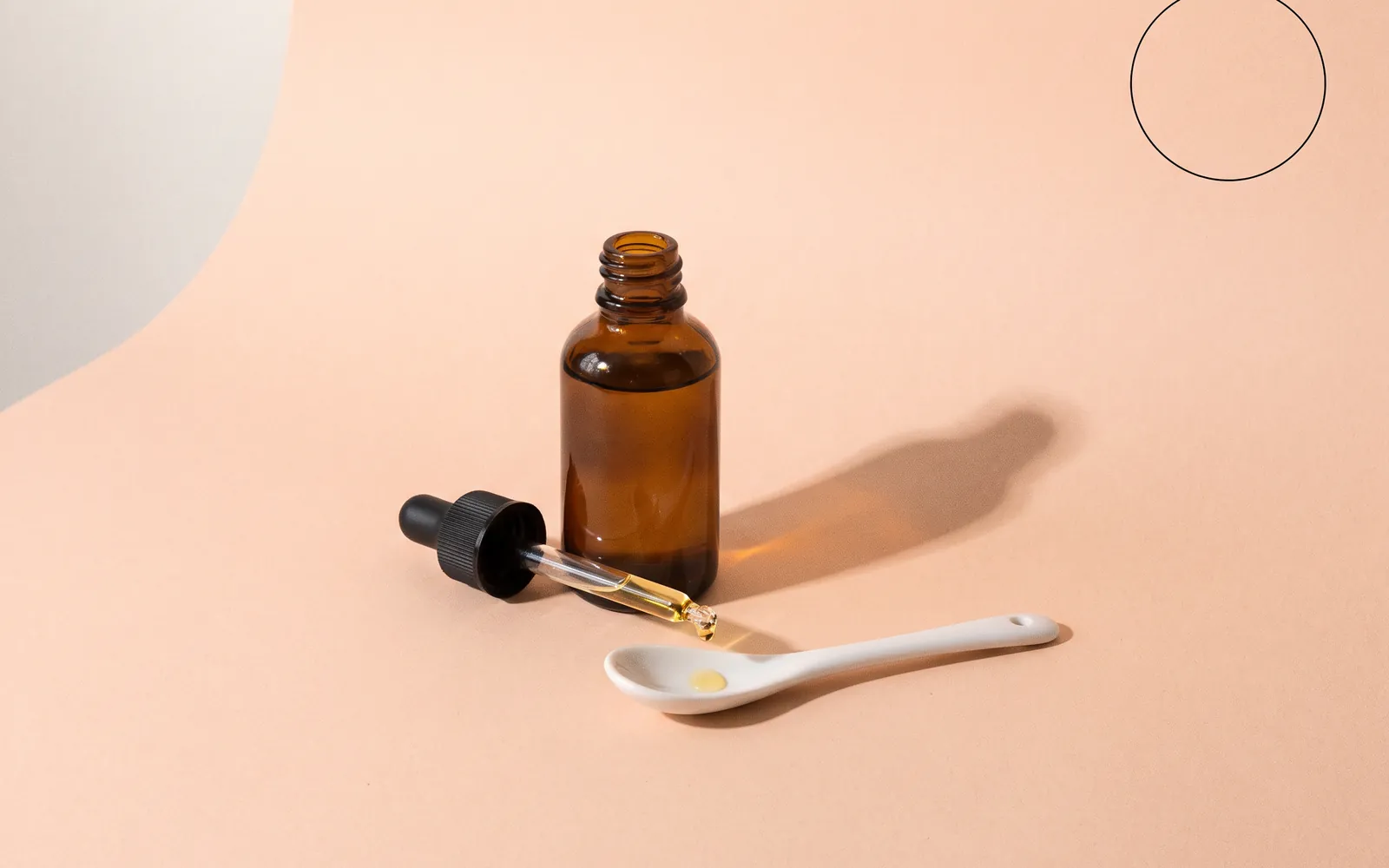 Stillleben: eine braune Glasflasche mit Pipette, aus der ein einzelner Tropfen fällt.
